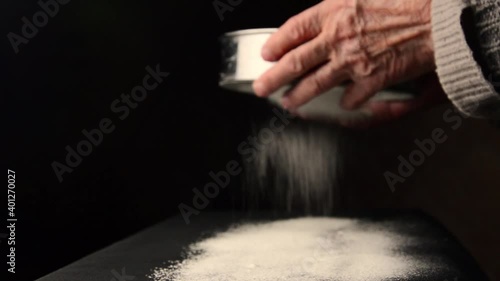 Old hands sift flour on a dark background close-up. An old mother sifting flour through a sieve on a dark background. A grandmother with a sieve in her hands sifts flour for baking bread.Bread concept