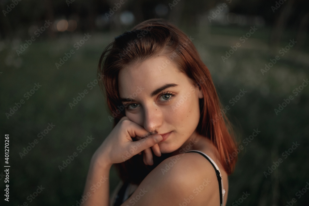 Medium shot portrait of young beautiful woman wearing a beige dress, posing in a field full of flowers and surrounded by trees. She is with her hand in her face. Medium shot portrait of young beautiful woman wearing a beige dress, posing in a field full of flowers and surrounded by trees. She is with her hand in her face.