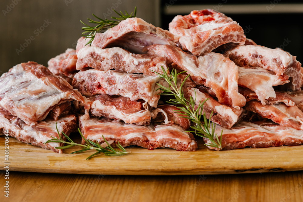 Heap of uncooked meat ribs with fat and aromatic rosemary sprigs on wooden table Heap of uncooked meat ribs with fat and aromatic rosemary sprigs on wooden table