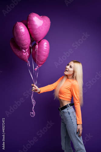 Happy blonde with heart-shaped balloons on a purple background in the studio. Valentine's Day. © vfhnb12