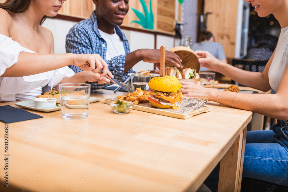 Positive young multiracial friends eating tasty dishes and burgers while gathering in modern restaurant Positive young multiracial friends eating tasty dishes and burgers while gathering in modern restaurant