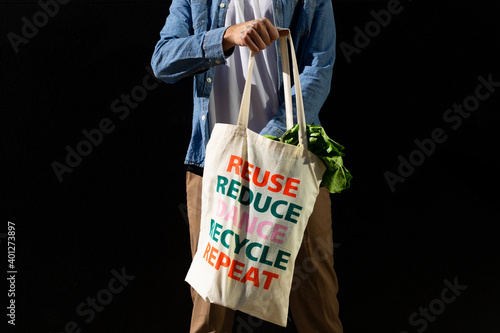 Crop anonymous male buyer holding fabric shopping bag with text message of reuse and recycle concept on black background