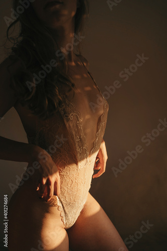 Side view of cropped unrecognizable curvy female wearing lace bodysuit standing in room lit by sunlight photo