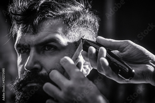 Hands of barber with hair clipper. Barber works with hair clipper. Hipster client getting haircut. Haircut concept. Man visiting hairstylist in barbershop. Black and white