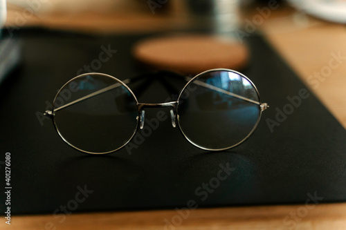 Classic eyeglasses of round shaped placed on black mat on blurred wooden desk photo