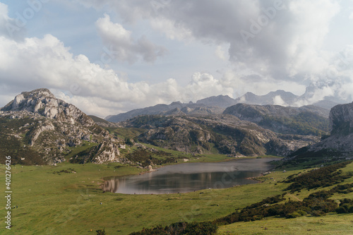 Amazing scenery of highland valley with abundant greenery and majestic rocky mountains surrounding tranquil pond