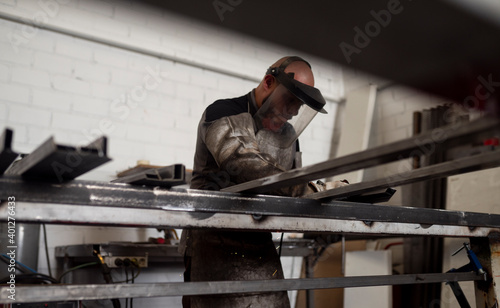 Serious male worker in dirty apron standing at workbench and preparing metal details for welding