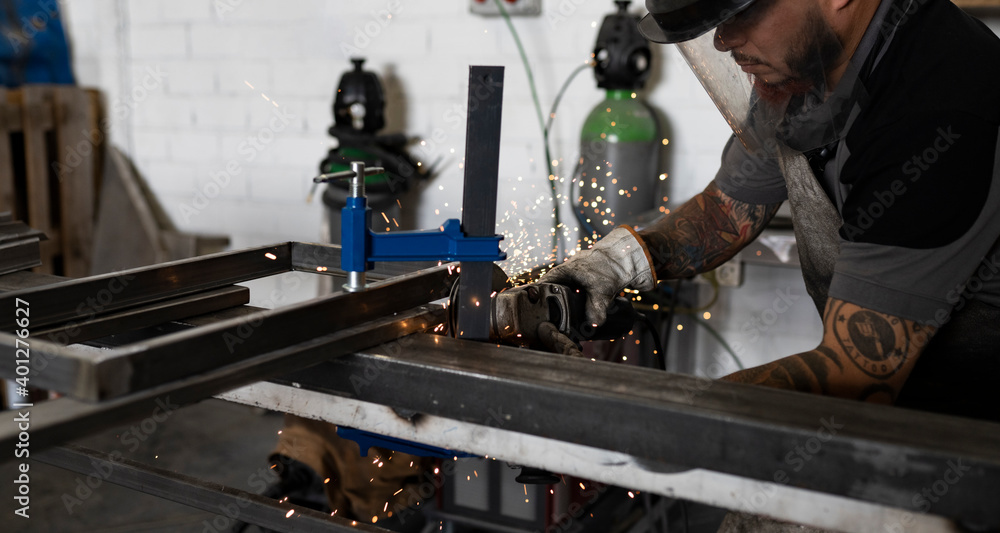 Side view of serious male welder using electric grinder and cutting metal detail in grungy workshop Side view of serious male welder using electric grinder and cutting metal detail in grungy workshop