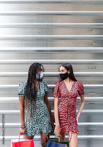 Wallpaper Mural Multiethnic female friends in protective masks and similar dresses standing on street with paper bags after shopping and looking at each other Torontodigital.ca