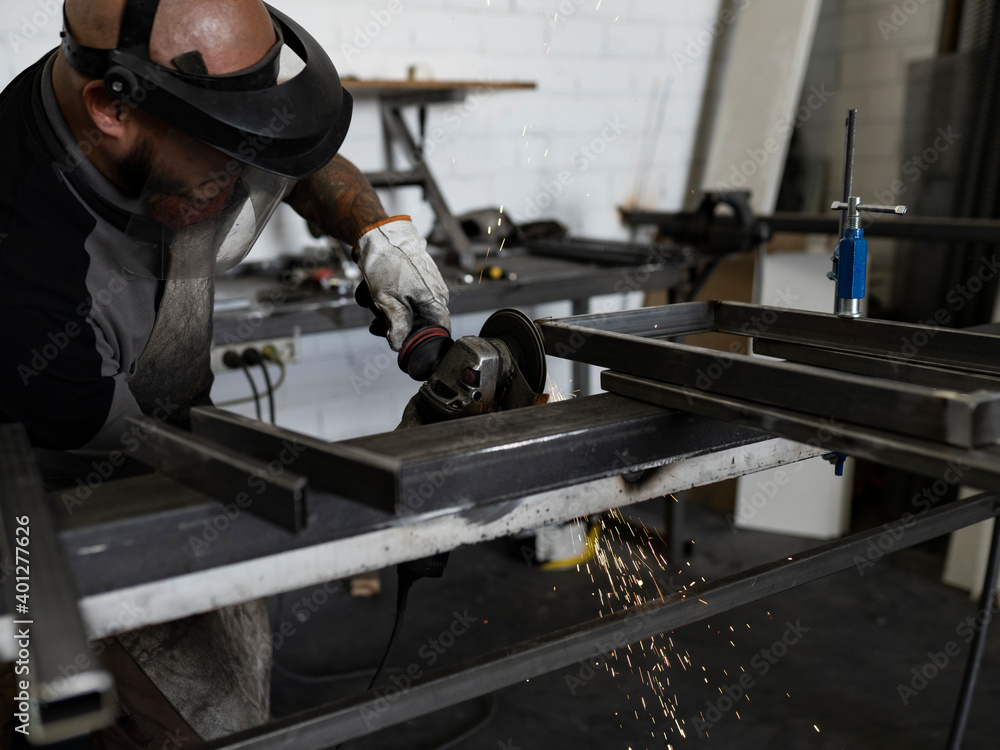 Side view of serious male welder using electric grinder and cutting metal detail in grungy workshop Side view of serious male welder using electric grinder and cutting metal detail in grungy workshop