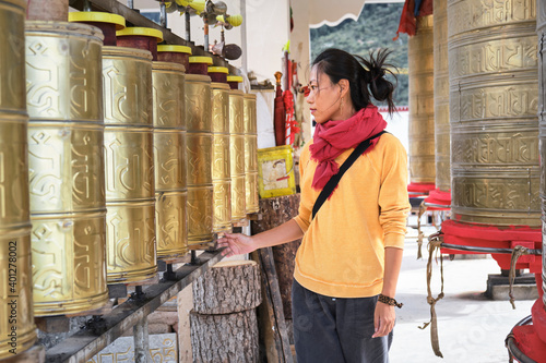 Side view of serious young ethnic female traveler in casual clothing with red headscarf watching at big golden Tibetan rolls in church photo