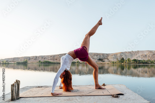 Young girl with red hair practicing yoga at the edge of a lake
