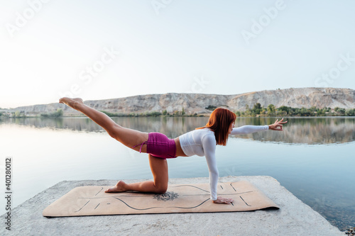 Young girl with red hair practicing yoga at the edge of a lake