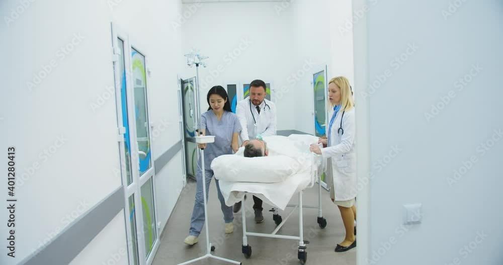 Emergency Department. Doctors, nurses and paramedics move patient lying on a stretcher through hospital corridors. Healthcare workers taking patient through a hall under lockdown. Covid-19 concept Emergency Department. Doctors, nurses and paramedics move patient lying on a stretcher through hospital corridors. Healthcare workers taking patient through a hall under lockdown. Covid-19 concept
