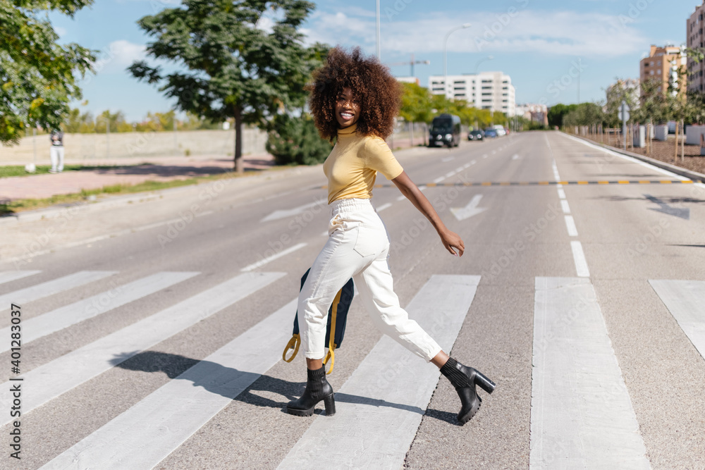 Black woman with afro hair crossing the street with a backpack in hand ...