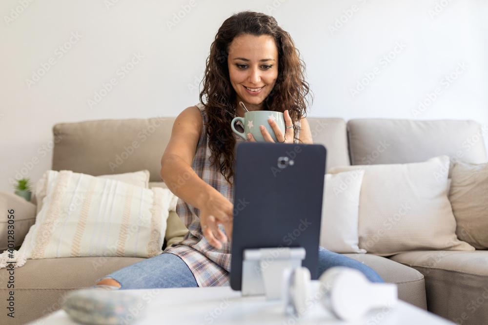 Content female in domestic outfit sitting on sofa with cup of coffee and watching movie on tablet while relaxing at weekend at home Content female in domestic outfit sitting on sofa with cup of coffee and watching movie on tablet while relaxing at weekend at home