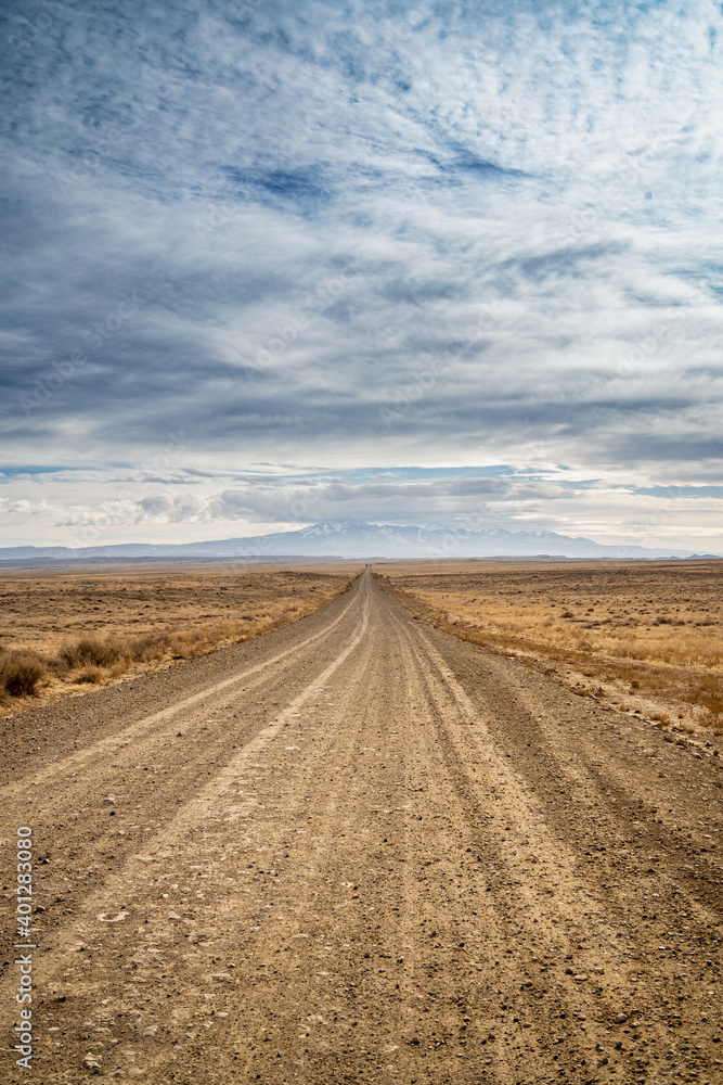 empty dirt road in the desert leading to mountains with blue sky and clouds