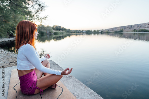 Young girl with red hair practicing meditation at the edge of a lake