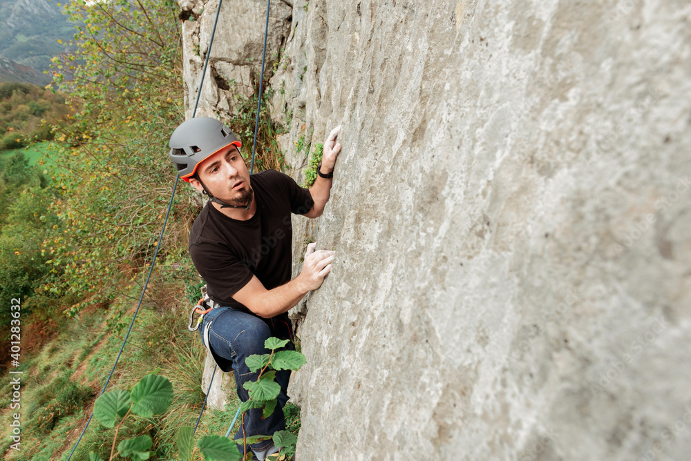 Sportive male alpinist climbing on sheer cliff in summer day Sportive male alpinist climbing on sheer cliff in summer day