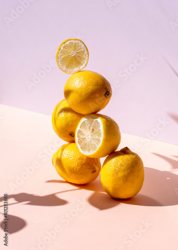 Creative composition of fresh lemons stacked in shape of pyramid on pink background in studio