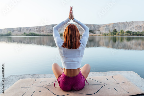 Young girl with red hair practicing meditation at the edge of a lake