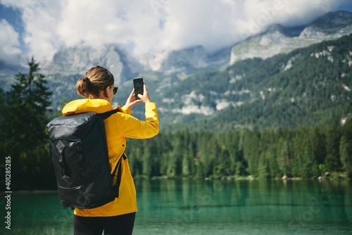 Back view of unrecognizable woman photographing high mountains on cellphone during trip in Dolomites