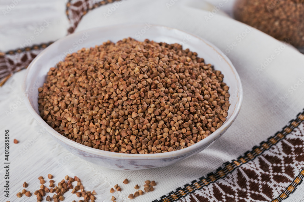 Bowl of dry raw buckwheat groats on a white wooden background. Cooking buckwheat porridge concept. Bowl of dry raw buckwheat groats on a white wooden background. Cooking buckwheat porridge concept.