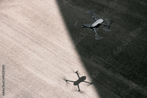From above modern drone flying in empty concrete walkway casting shadows on sunny day