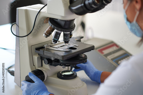 Crop unrecognizable female specialist in uniform with medical sample near microscope at work in laboratory photo