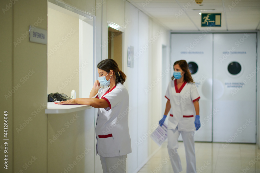 Unrecognizable medical staff talking on telephone near female partner in uniform walking in hospital corridor with paper Unrecognizable medical staff talking on telephone near female partner in uniform walking in hospital corridor with paper