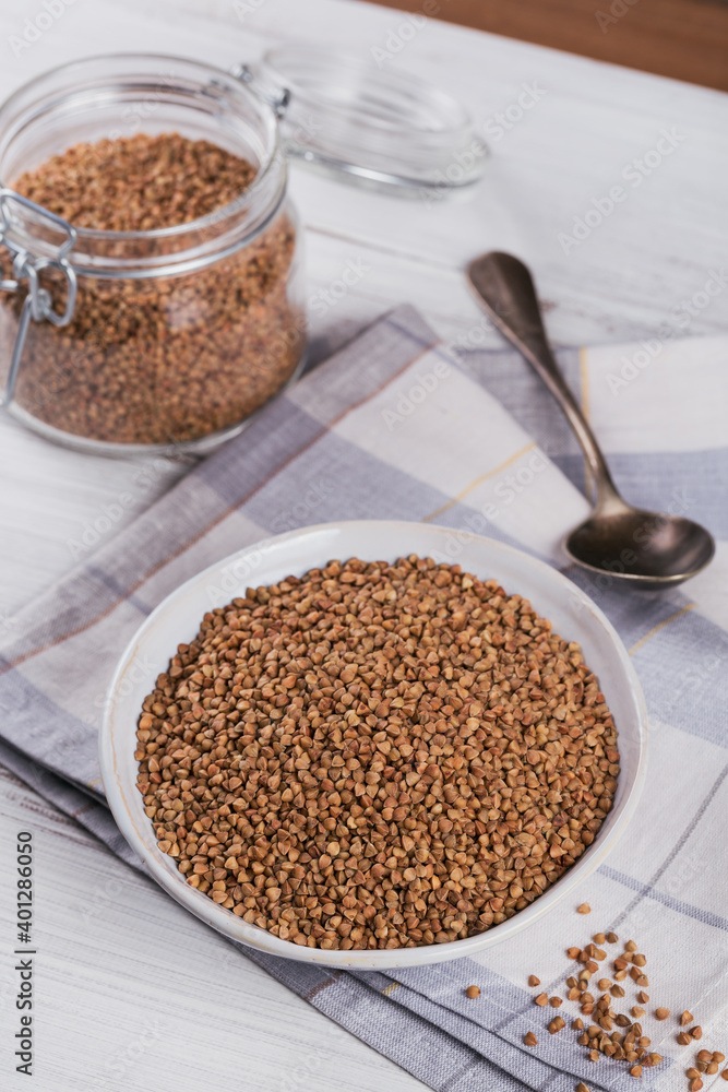 Bowl of dry raw buckwheat groats on a white wooden background. Cooking buckwheat porridge concept. Bowl of dry raw buckwheat groats on a white wooden background. Cooking buckwheat porridge concept.