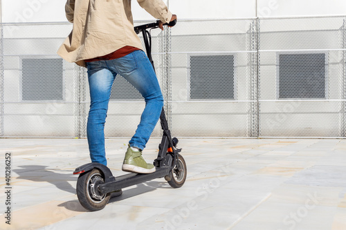 Back view of faceless ethnic male standing on modern electric scooter near metal wall on sunny day in city photo