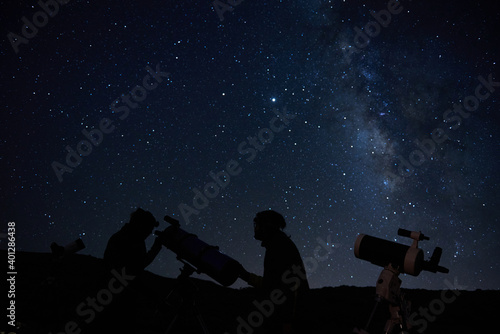Silhouettes of anonymous scientists using telescopes while exploring night starry sky with milky way in darkness photo