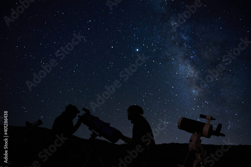 Silhouettes of anonymous scientists using telescopes while exploring night starry sky with milky way in darkness