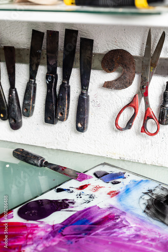 Various chisels and scissors arranged on wall near table with paints on workplace in engraving workshop photo