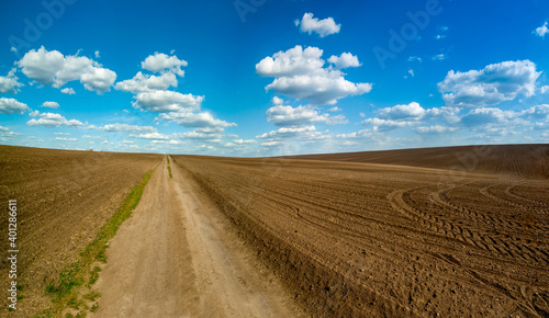 plowed field and dirt road in spring, beautiful blue sky with clouds