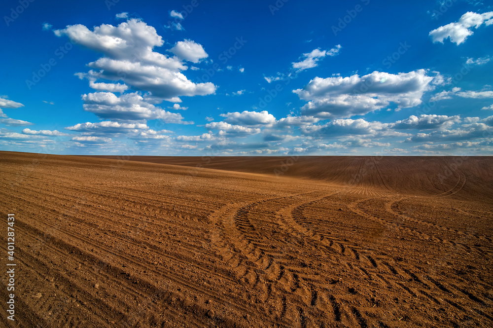 plowed field, tracks of tractor tires, beautiful blue sky with clouds plowed field, tracks of tractor tires, beautiful blue sky with clouds