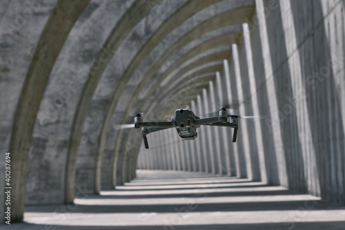 Modern drone flying in empty arched walkway with columns casting shadows in shape of lines on sunny day photo