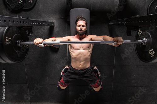 From above of strong focused male athlete lying on bench press and doing exercises with heavy barbell during workout in gym