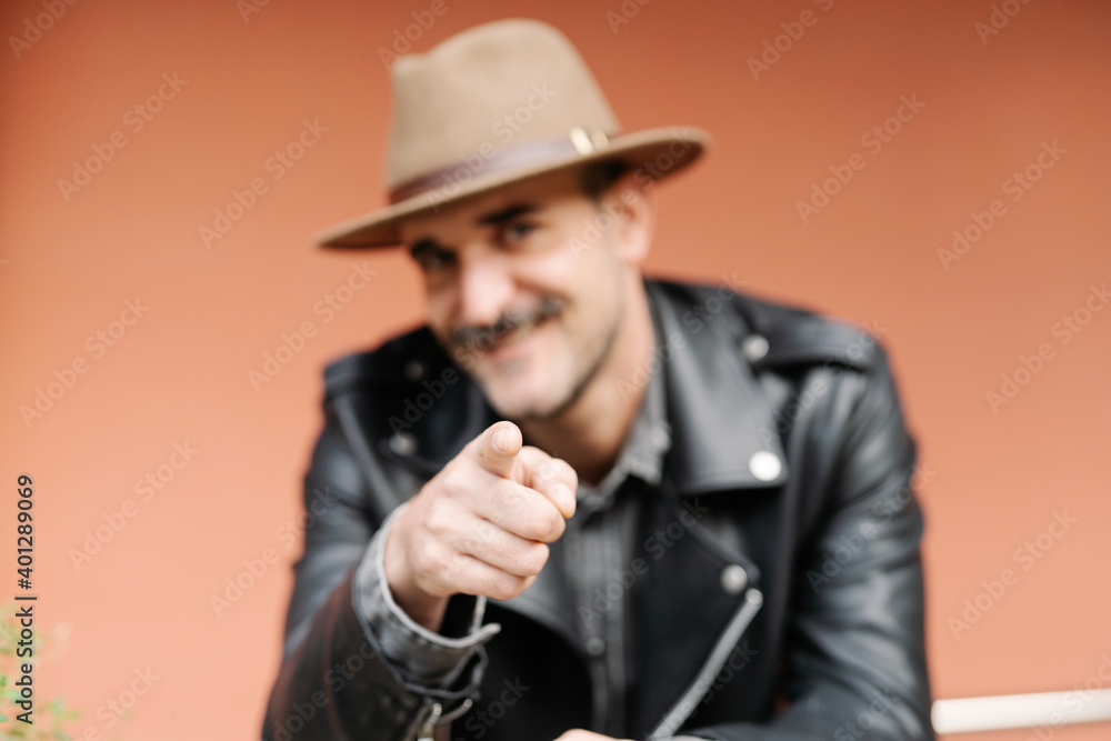 Happy charismatic bearded blurred male in hat looking at camera near beige wall Happy charismatic bearded blurred male in hat looking at camera near beige wall