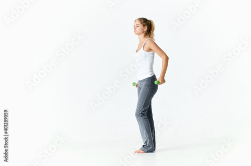 woman goes in for sports with dumbbells in a bright room and gray pants