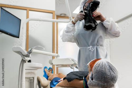 Unrecognizable professional dentist using portable X ray device for examining teeth of patient in protective goggles while working in modern dental clinic photo