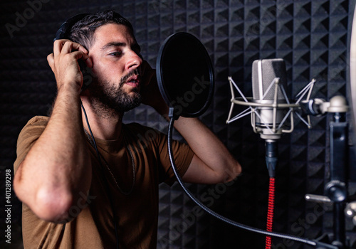 Side view of male singer in headphones standing in acoustic room with soundproof walls and microphone and recording song in studio photo