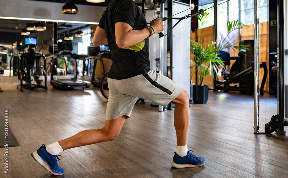 Side view of strong male lifting heavy weights on exercise machine while standing in lunge posture Side view of strong male lifting heavy weights on exercise machine while standing in lunge posture