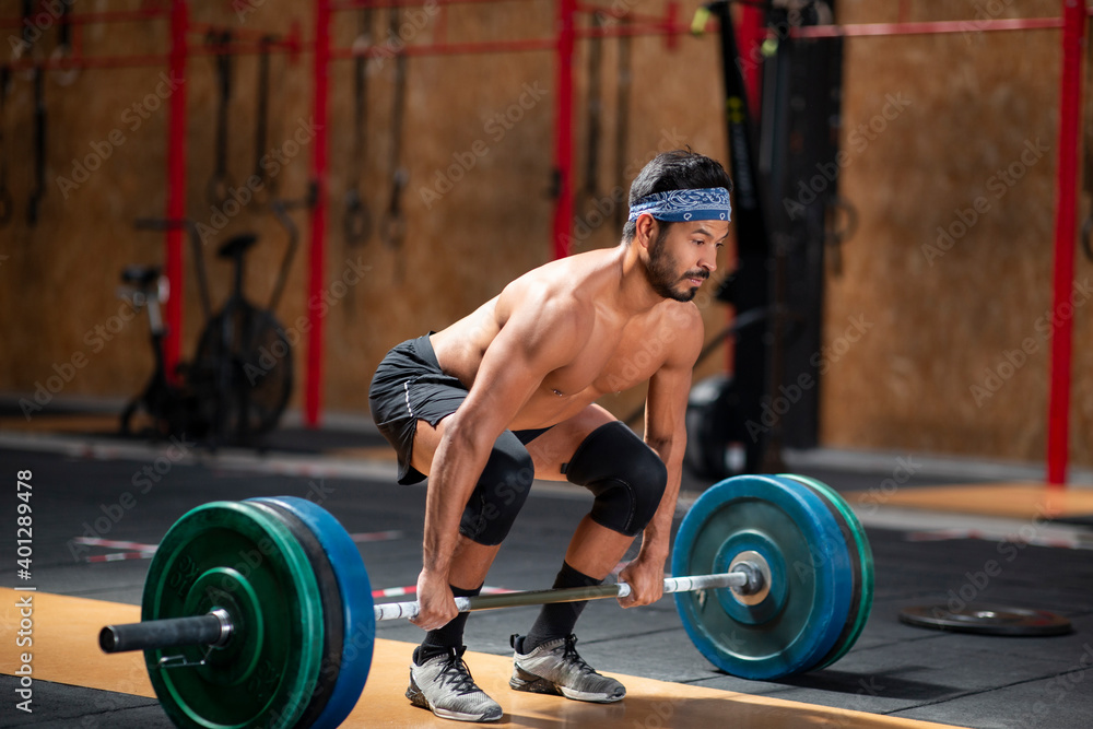 Concentrated male athlete lifting heavy barbell during weightlifting workout in gym while looking away Concentrated male athlete lifting heavy barbell during weightlifting workout in gym while looking away
