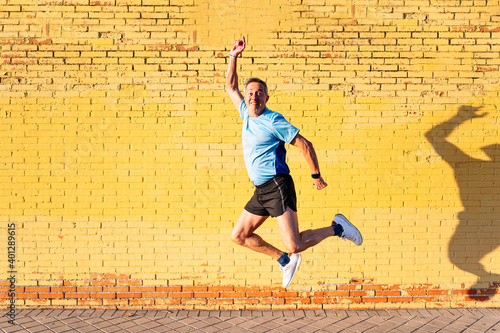 Senior retired man athlete jumping on yellow background