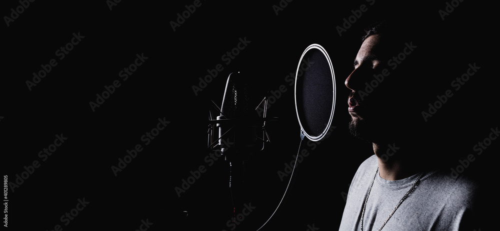 Talented male singer recording music in front of modern microphone in dark studio
