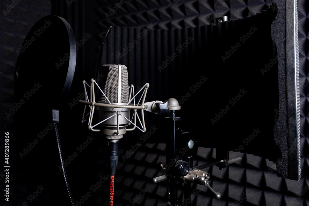 Contemporary metal microphone with wire placed on background of soundproof foam with pyramid shaped pattern in dark music recording studio Contemporary metal microphone with wire placed on background of soundproof foam with pyramid shaped pattern in dark music recording studio