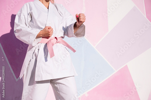 Cropped unrecognizable determined mature woman in pink head cover and belt fighting karate in cancer battle concept in the street on pink wall photo