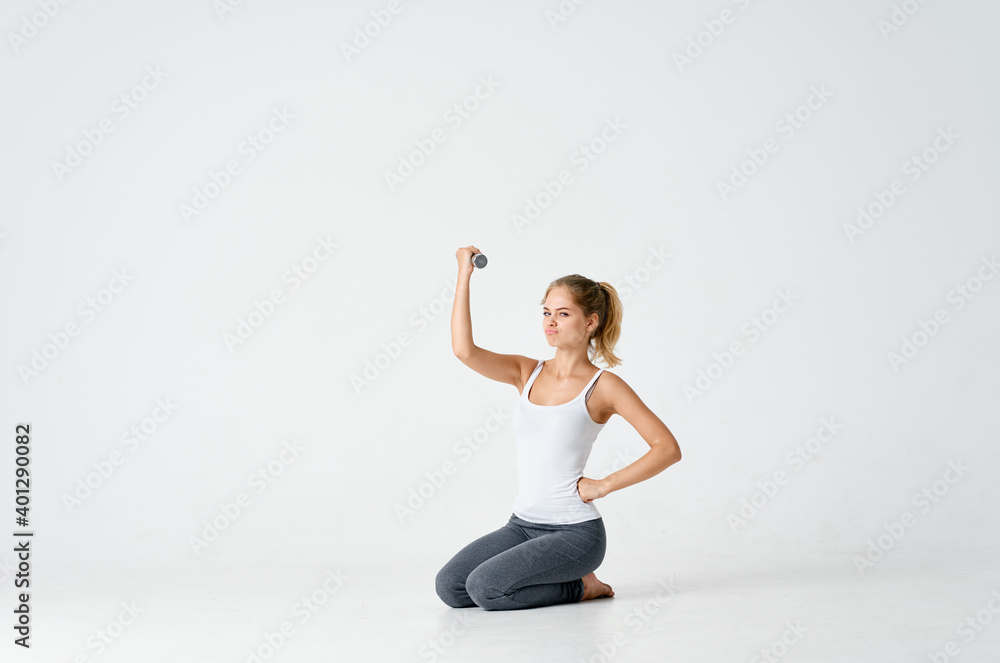 woman in sweatpants sits on the floor with dumbbells in hands Fitness